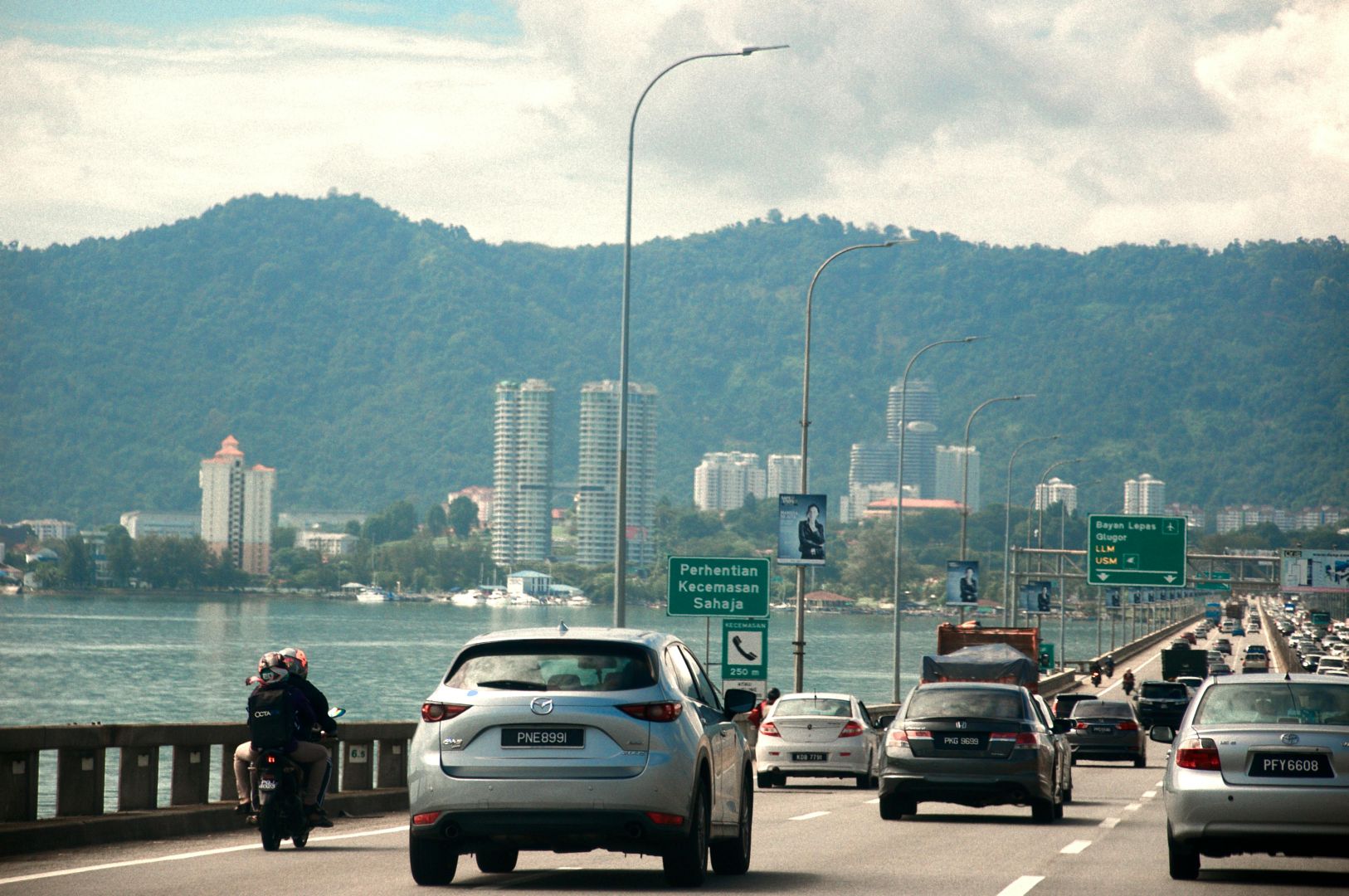 Blick auf den geschäftigen Verkehr auf der Penang-Brücke vor einer Bergkulisse in Malaysia.