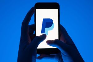 Eine Frau hält ein Smartphone mit dem Paypal Logo