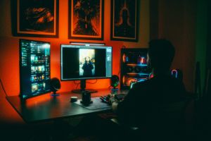 Eine Person bearbeitet nachts Fotos in einem neonbeleuchteten Heimbüro mit zwei Bildschirmen.
