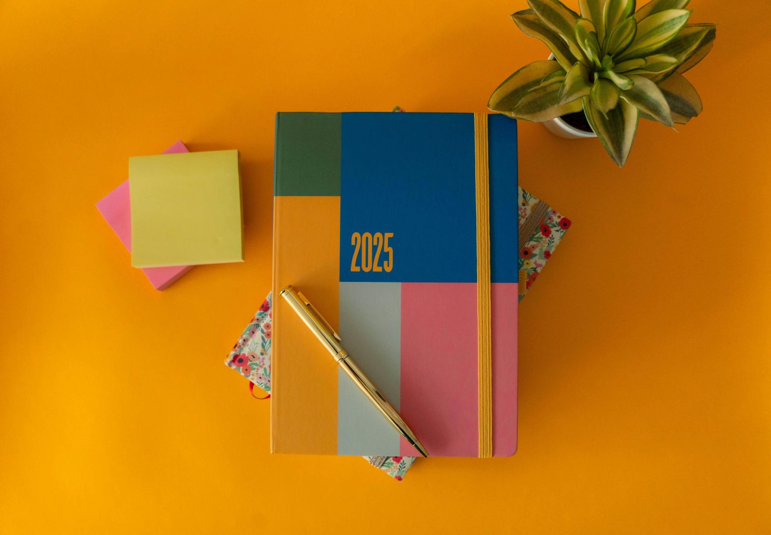 Flache Darstellung eines lebendigen Planers für 2025 mit einem Stift und einer grünen Pflanze auf gelbem Hintergrund.