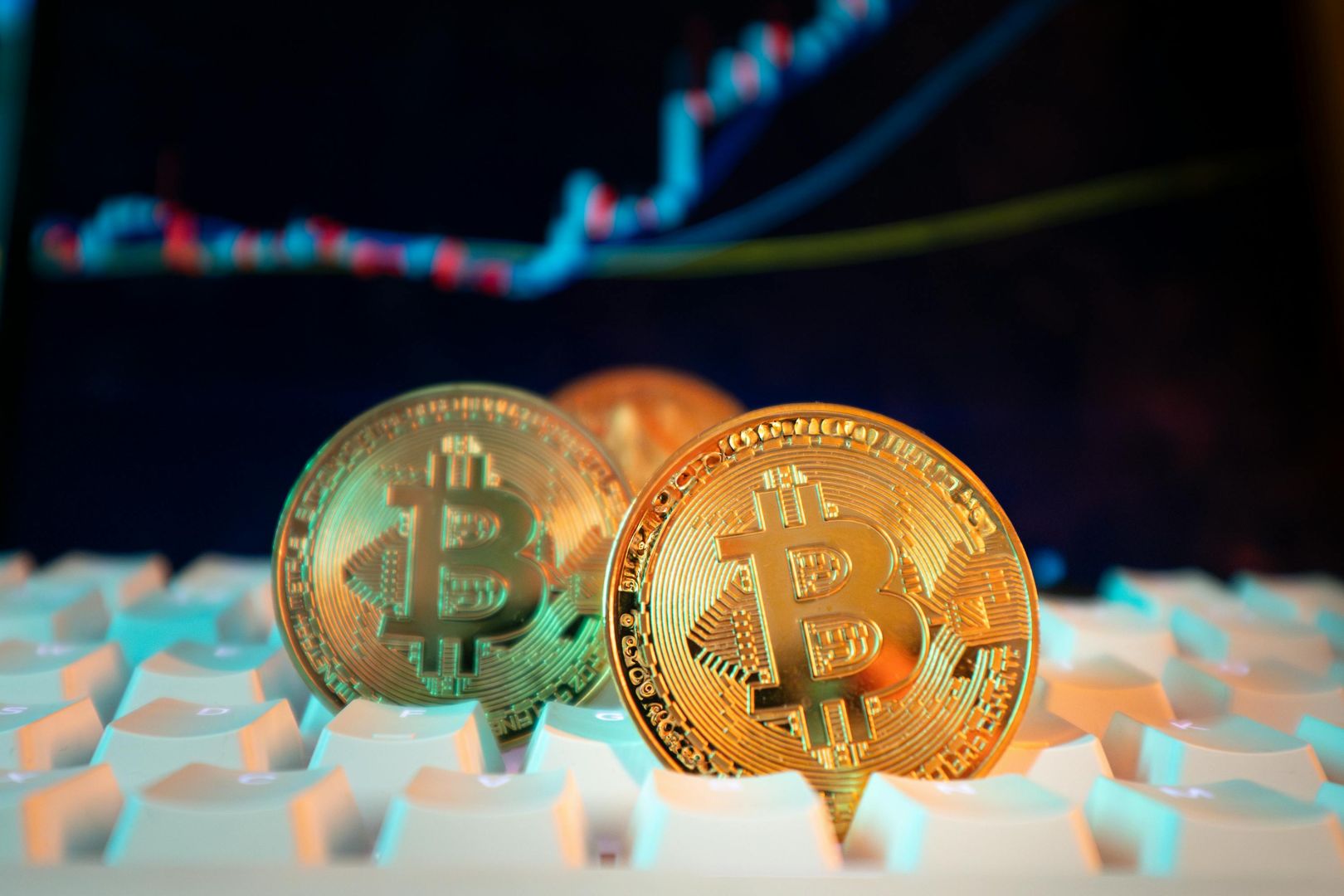 Goldene Bitcoin-Münzen auf einer Tastatur mit einem Finanzdiagramm im Hintergrund, das digitale Währungen und Markttrends darstellt.