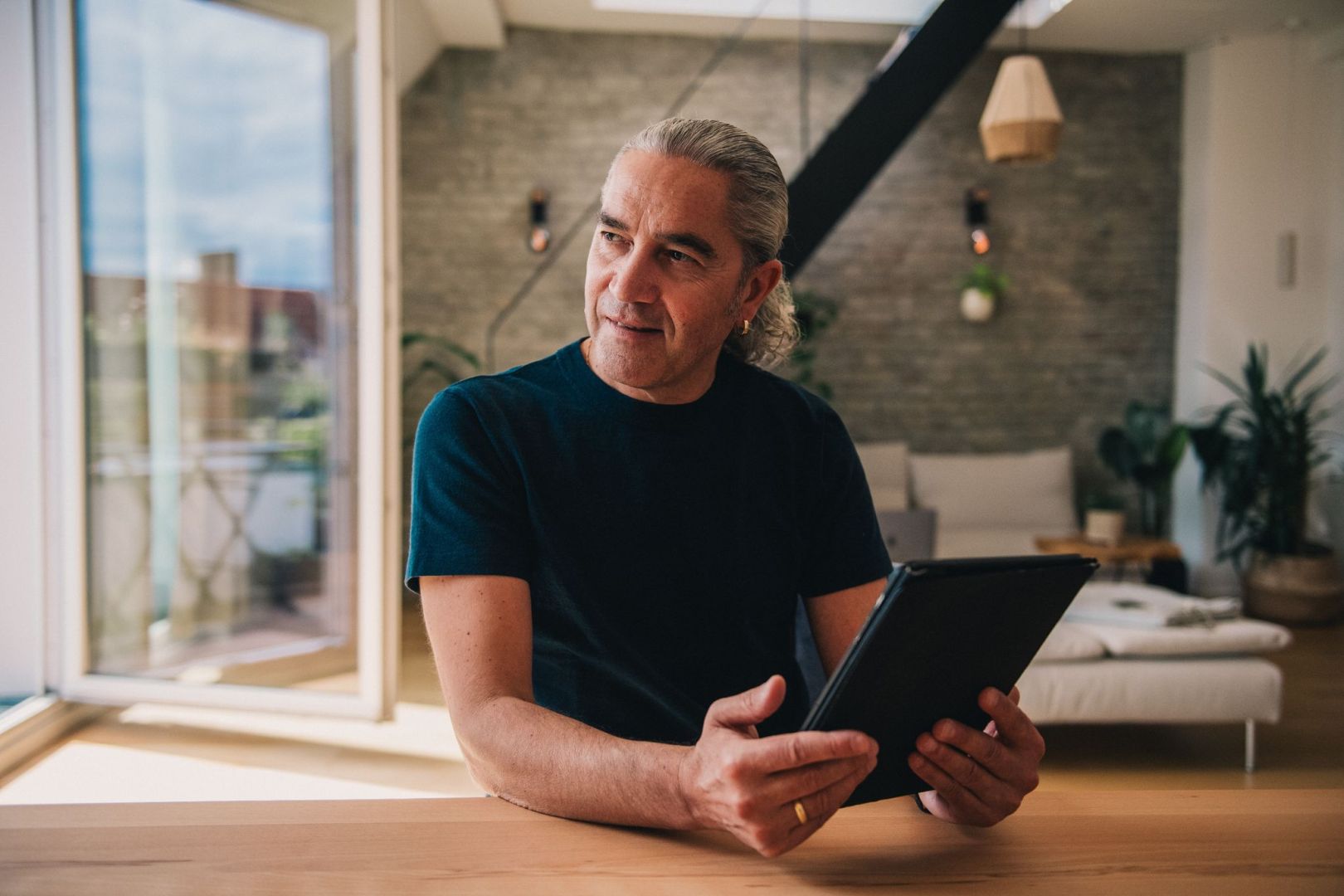 Mann sitzt in seiner Wohnung mit einem Tablet in der Hand