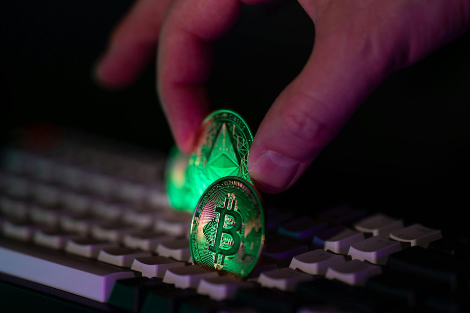 Nahaufnahme einer Hand, die Bitcoin- und Ethereum-Münzen auf eine Computertastatur legt, als Symbol für Kryptowährung und digitale Finanzen.