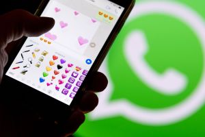 Smartphone mit Emojis aus WhatsApp vor dem WhatsApp-Logo