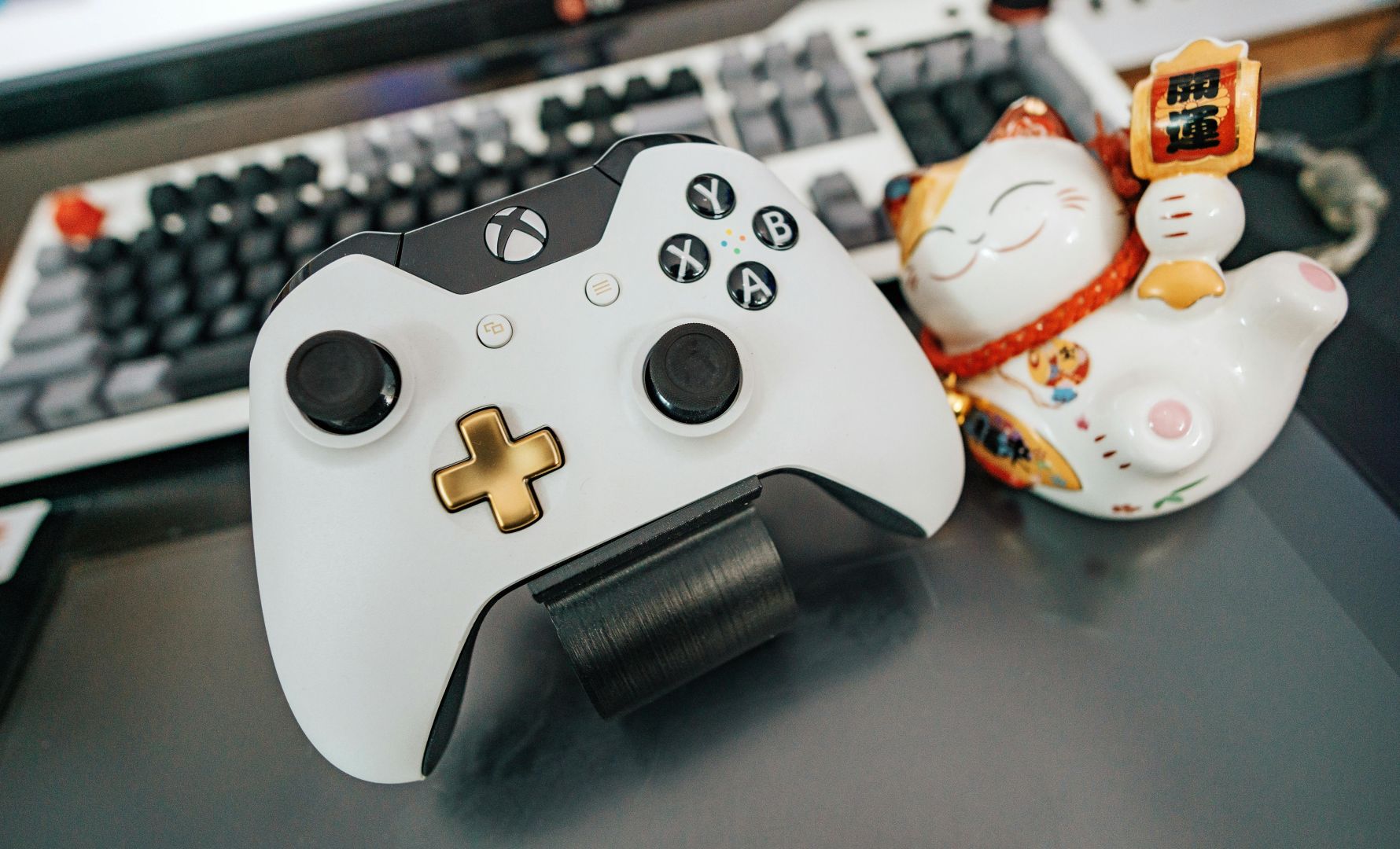 Weißer Und Schwarzer Xbox One Wireless Controller Neben Weißer Und Mehrfarbiger Keramikkatzenfigur Auf Schwarzer Oberfläche