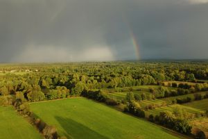 Atemberaubende Luftaufnahme einer lebendigen schwedischen Landschaft mit Regenbogen und stürmischem Himmel.