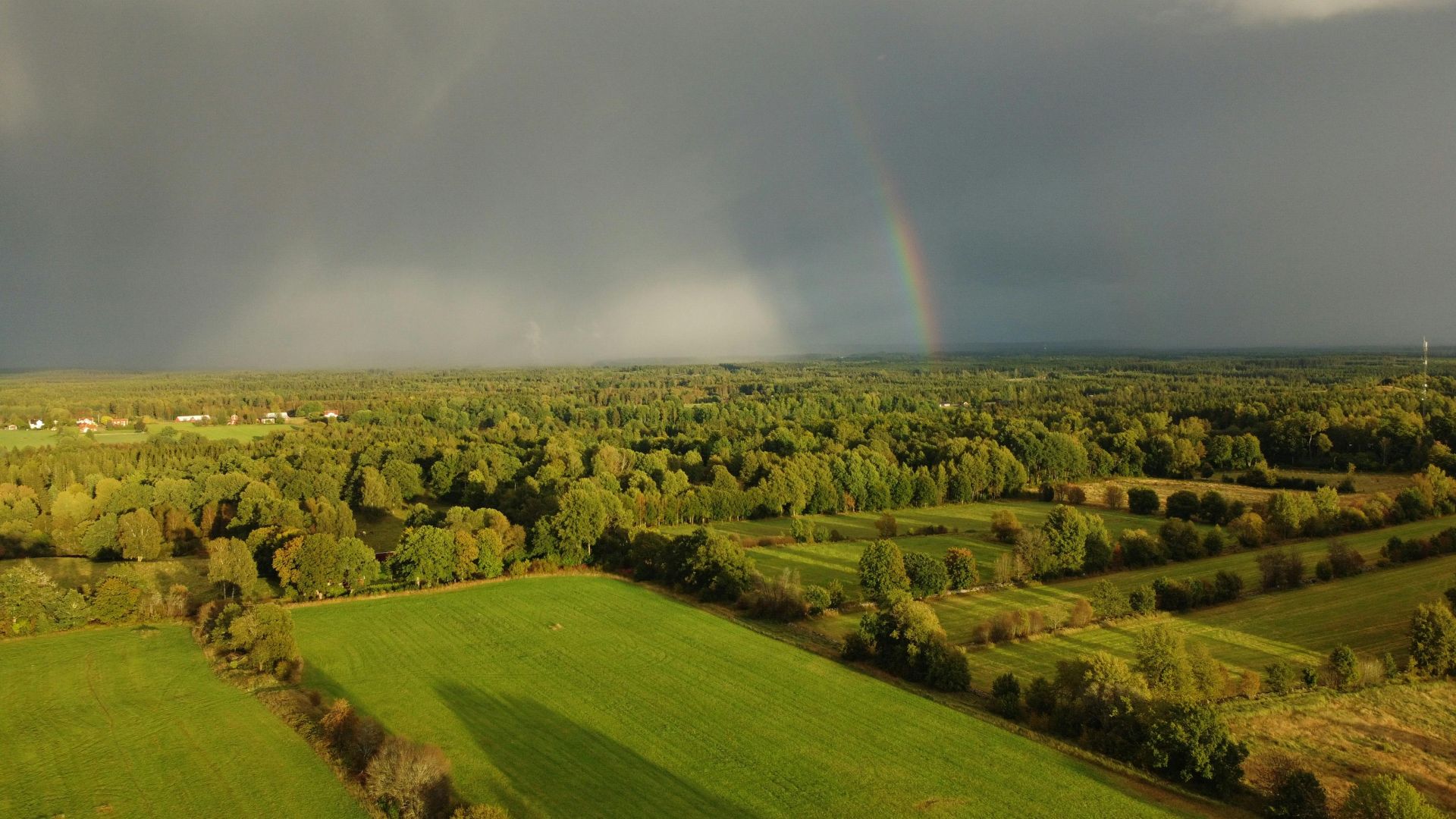 Atemberaubende Luftaufnahme einer lebendigen schwedischen Landschaft mit Regenbogen und stürmischem Himmel.