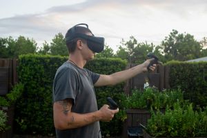 Außenszene eines Mannes, der ein Virtual-Reality-Headset und Controller verwendet und in ein virtuelles Spiel vertieft ist.