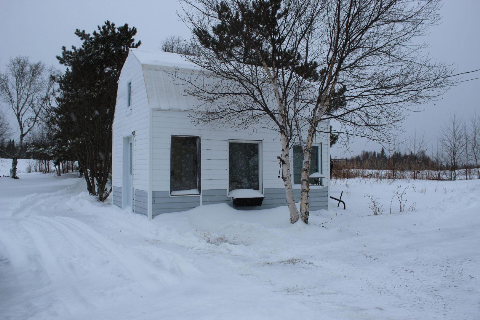 Ein kleines, von Schnee umgebenes Haus in ruhiger, ländlicher Winterlandschaft.