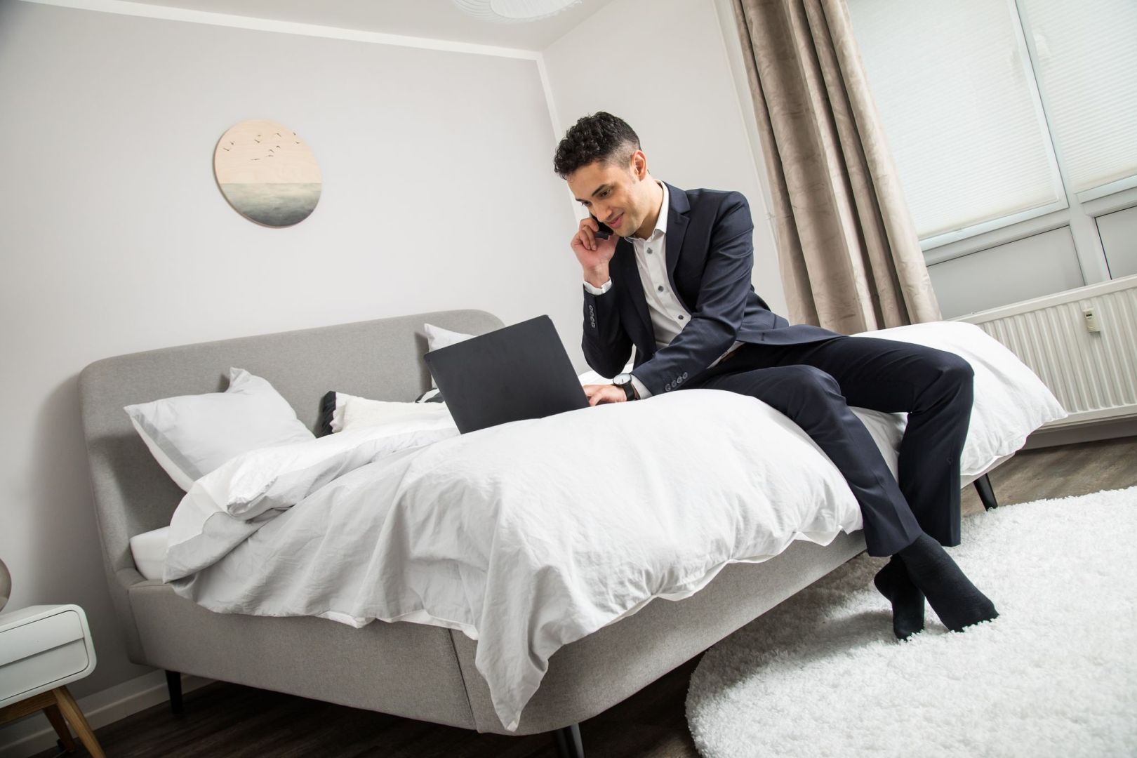 Ein Mann im Anzug sitzt auf einem Bett vor seinem Laptop