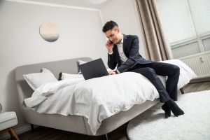 Ein Mann im Anzug sitzt auf einem Bett vor seinem Laptop