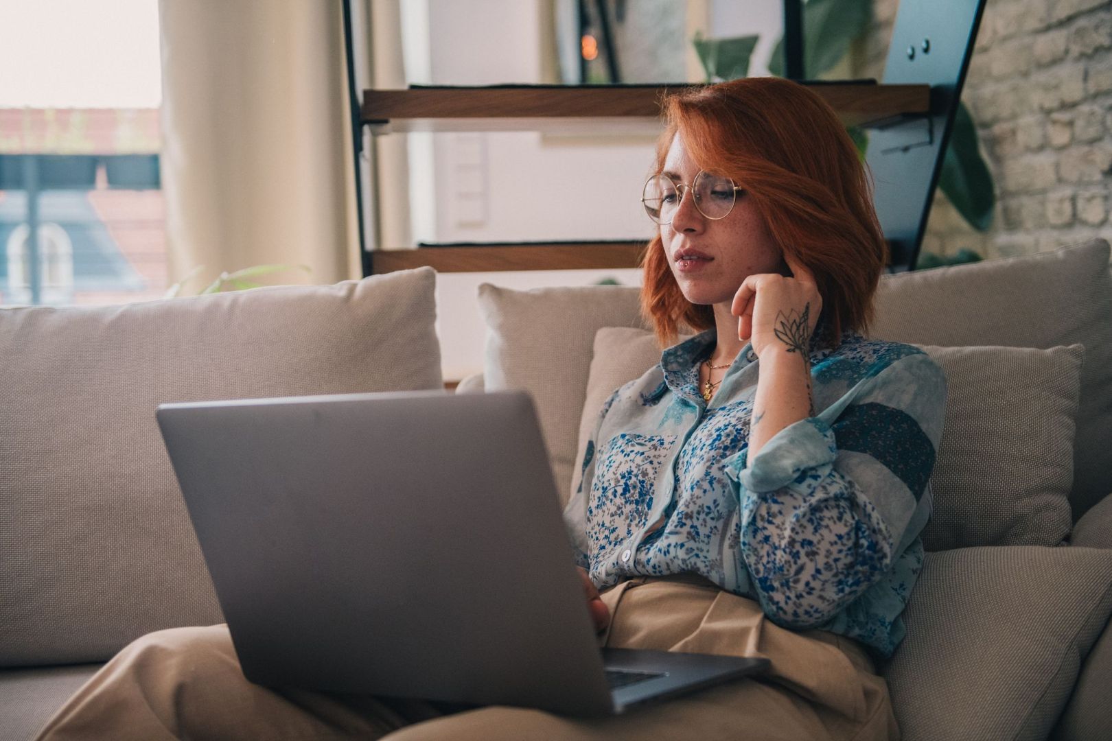 Eine Frau sitzt auf der Couch und nutzt einen Laptop