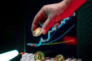Eine Hand hält Kryptowährungsmünzen, im Hintergrund ist ein Finanzdiagramm zu sehen, das Markttrends darstellt.