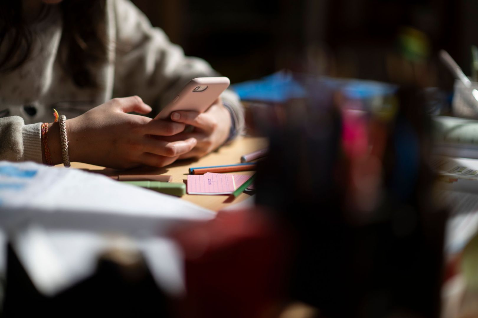 Eine Jugendliche sitzt mit Smartphone an einem Schreibtisch