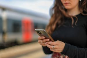 Eine junge Frau steht mit ihrem Mobiltelefon auf einem Bahnsteig
