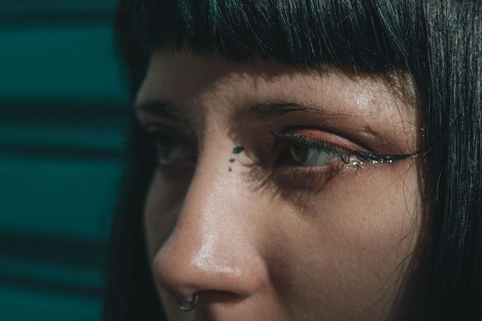 Eine Nahaufnahme einer Person mit Glitzer-Augen-Make-up und einem Nasenring.