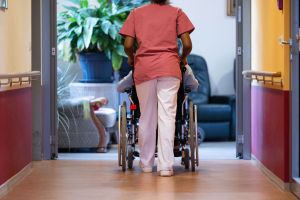 Eine Pflegekraft schiebt einen Pflegebedürftigen im Rollstuhl