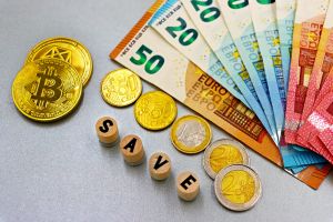 Euro-Banknoten und Bitcoin-Münzen mit dem Text „Speichern“ für ein Finanzkonzept.