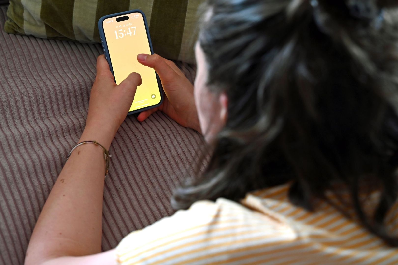 Frau liegt auf dem Sofa und schaut auf ein Smartphone