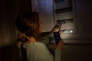 Frau schaut während eines Stromausfalls in den Sicherungskasten