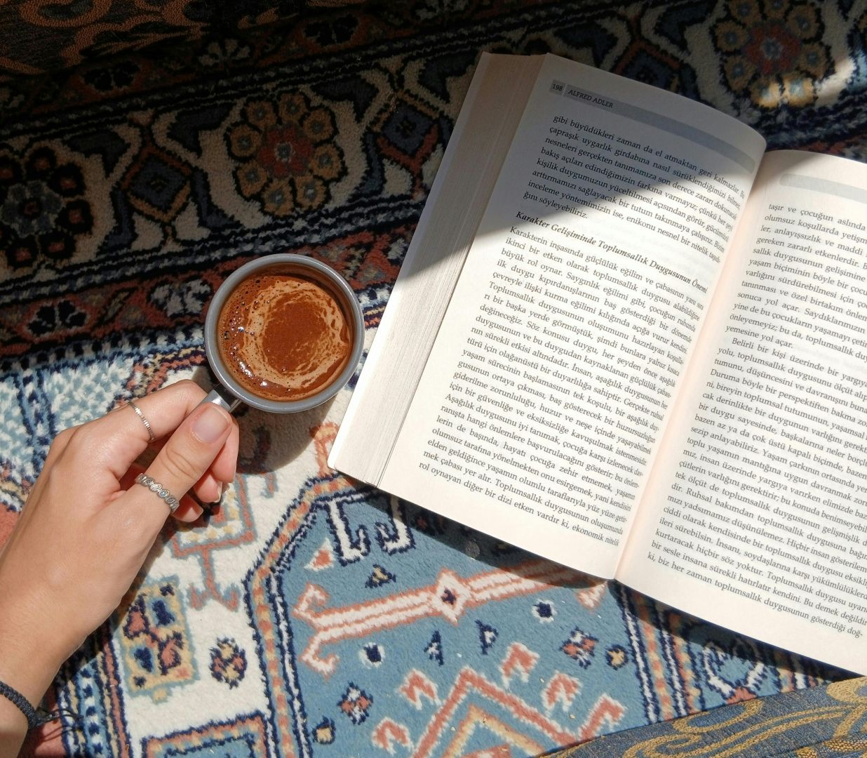 Genießen Sie einen warmen Kaffee und lesen Sie dabei auf einem gemusterten Teppich im Sonnenlicht.