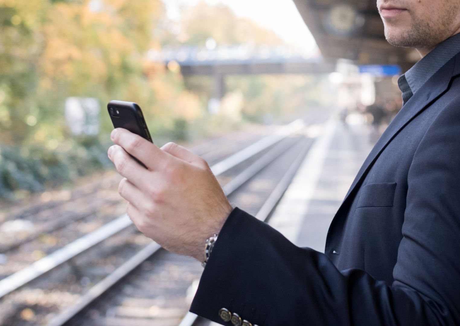 Mann mit Smartphone am Gleis