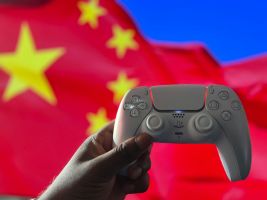 Nahaufnahme einer Hand, die einen PlayStation-Controller vor einer chinesischen Flagge hält. Aufgenommen in London, Großbritannien.