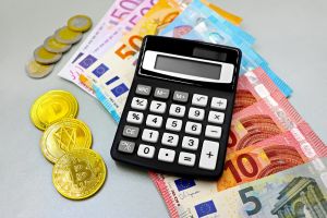 Taschenrechner mit Euro-Banknoten und Kryptowährungsmünzen wie Bitcoin auf einem Tisch.