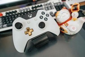 Weißer Und Schwarzer Xbox One Wireless Controller Neben Weißer Und Mehrfarbiger Keramikkatzenfigur Auf Schwarzer Oberfläche